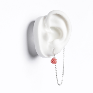 White ear mould shows child's earring in pink rose flower earring with silver chain